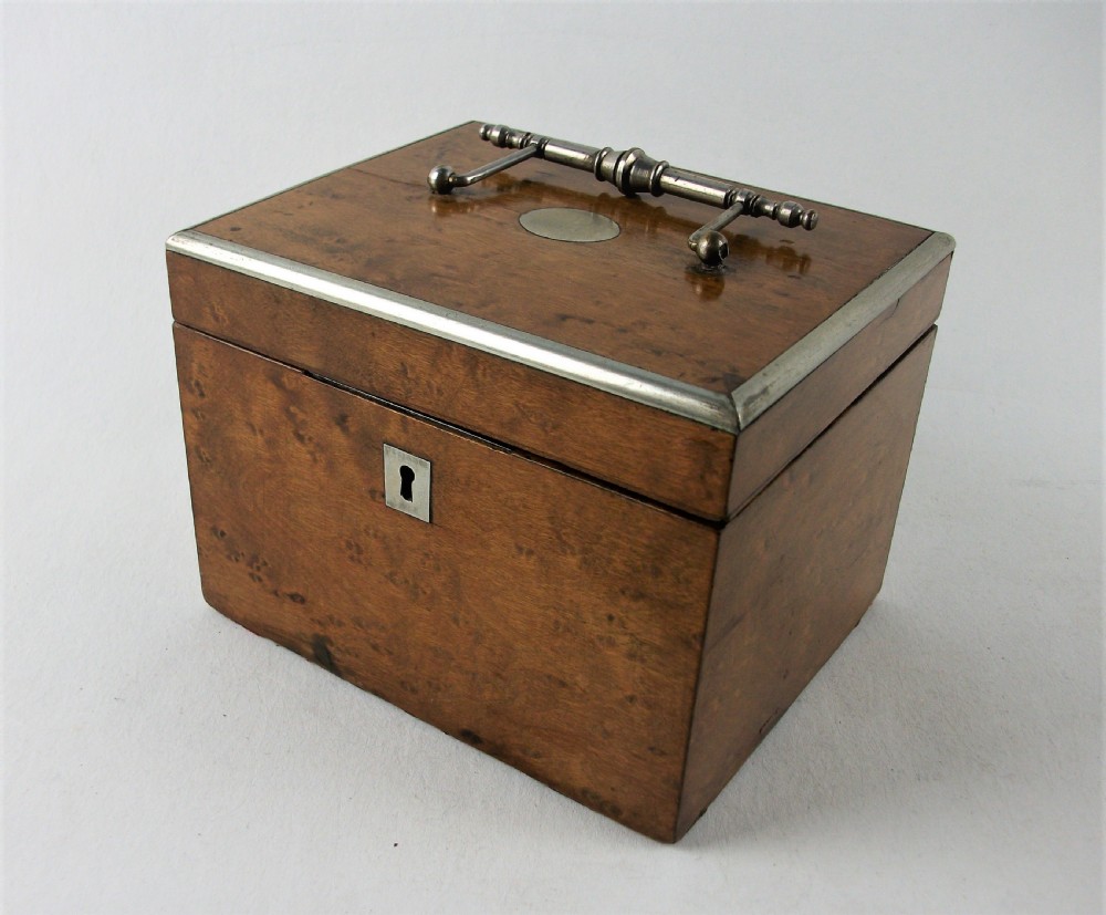 A rectangular antique burr maple wooden tea caddy featuring metal trim, a lid handle, an oval central cartouche, and a keyhole escutcheon.