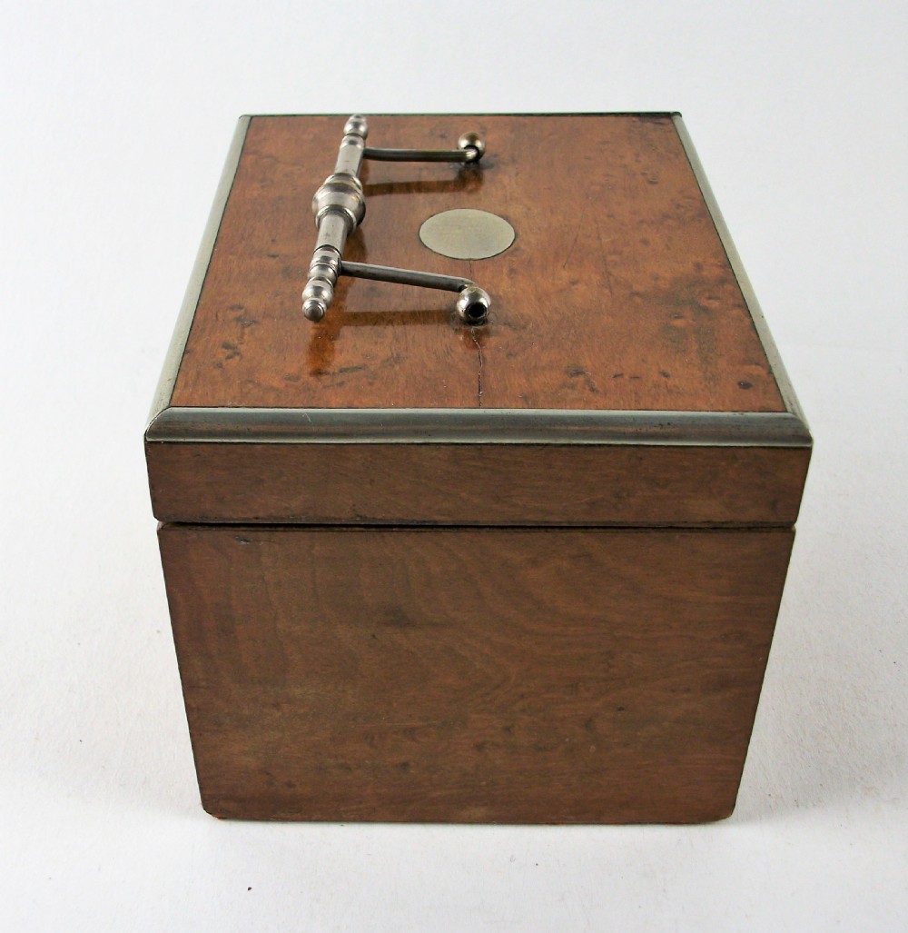 A rectangular antique burr maple wooden tea caddy featuring metal trim, a lid handle, an oval central cartouche, and a keyhole escutcheon. View X