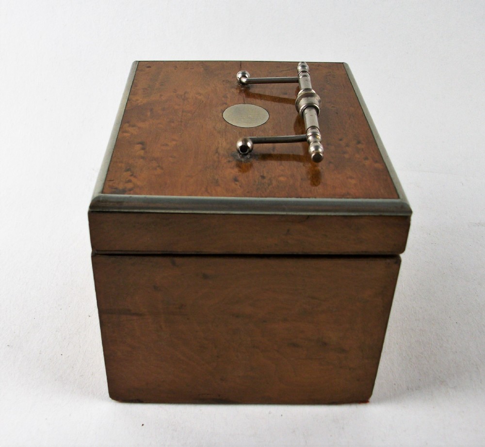 A rectangular antique burr maple wooden tea caddy featuring metal trim, a lid handle, an oval central cartouche, and a keyhole escutcheon. View VI