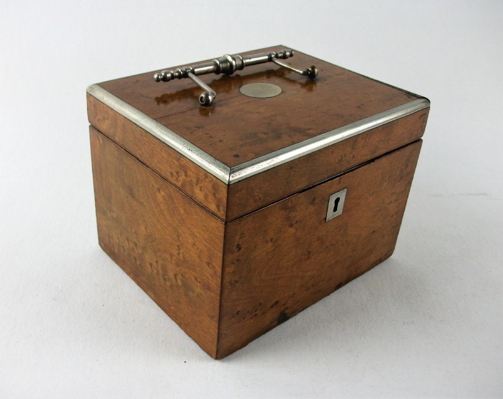 A rectangular antique burr maple wooden tea caddy featuring metal trim, a lid handle, an oval central cartouche, and a keyhole escutcheon. View VII