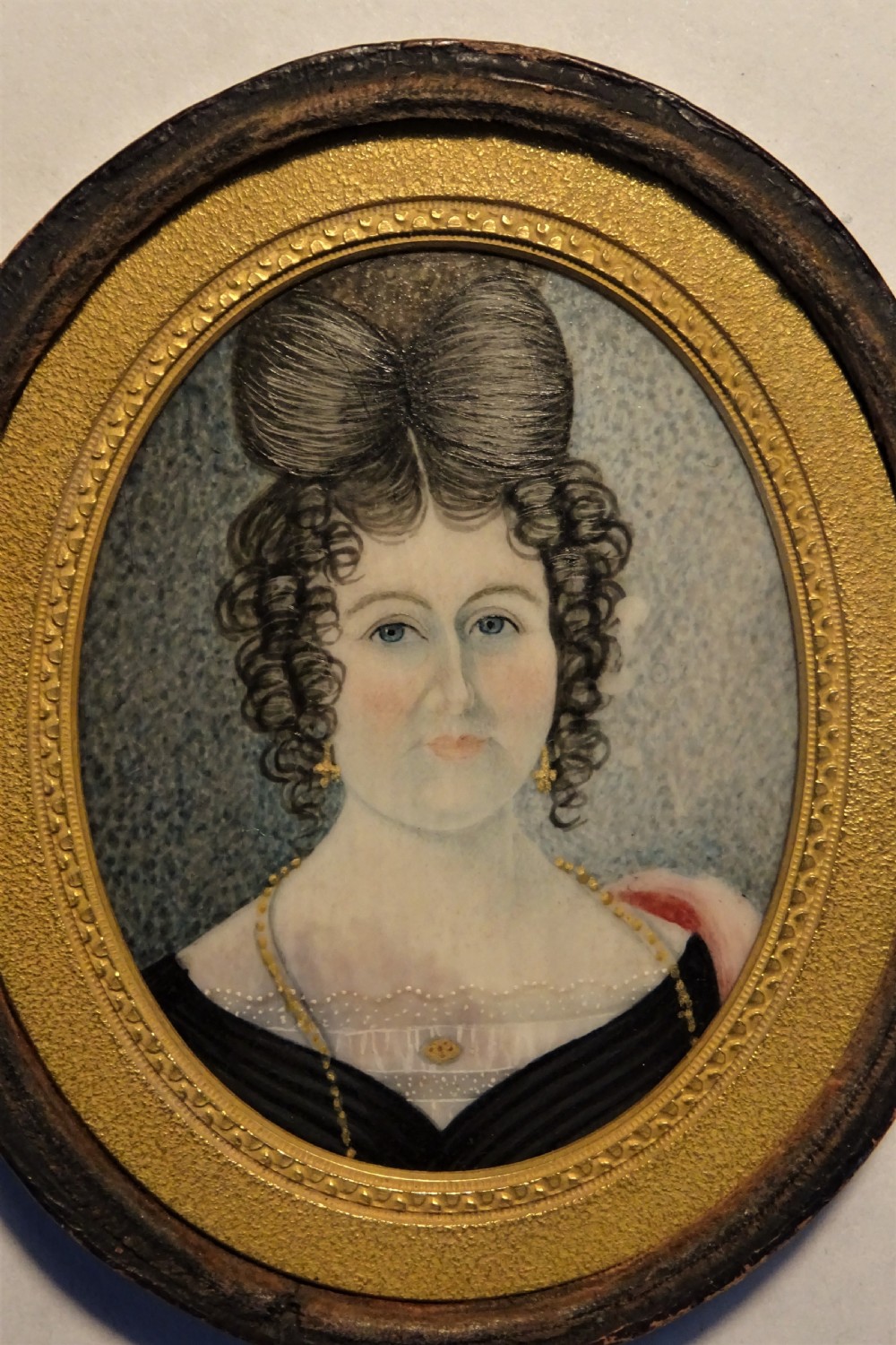 An oval Georgian portrait miniature depicting a lady with elaborate dark hair in an ornate gilt inner border and dark wooden frame. View XIII