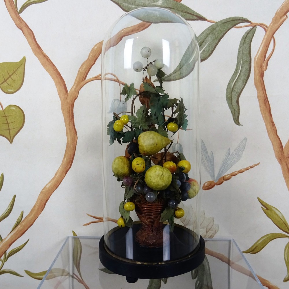 A 19th-century glass cloche dome enclosing an arrangement of wax pears, apples, and grapes set in a small woven basket on an ebonised wooden base.