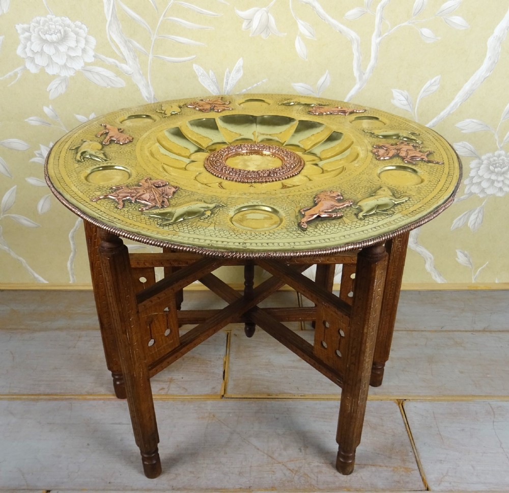A circular engraved brass tray table with copper reliefs set upon a folding wooden base with a matching brass ewer and goblets. View IX