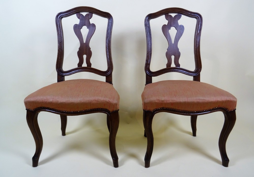 A pair of mid-18th century Italian walnut side chairs featuring carved openwork backsplats, moulded crest rails, fabric upholstered seats, and cabriole legs.