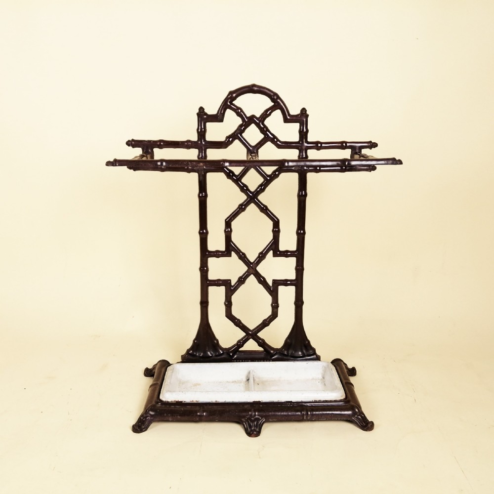 A dark cast iron Victorian umbrella stand featuring a faux bamboo lattice structure and a white painted drip tray at the base.