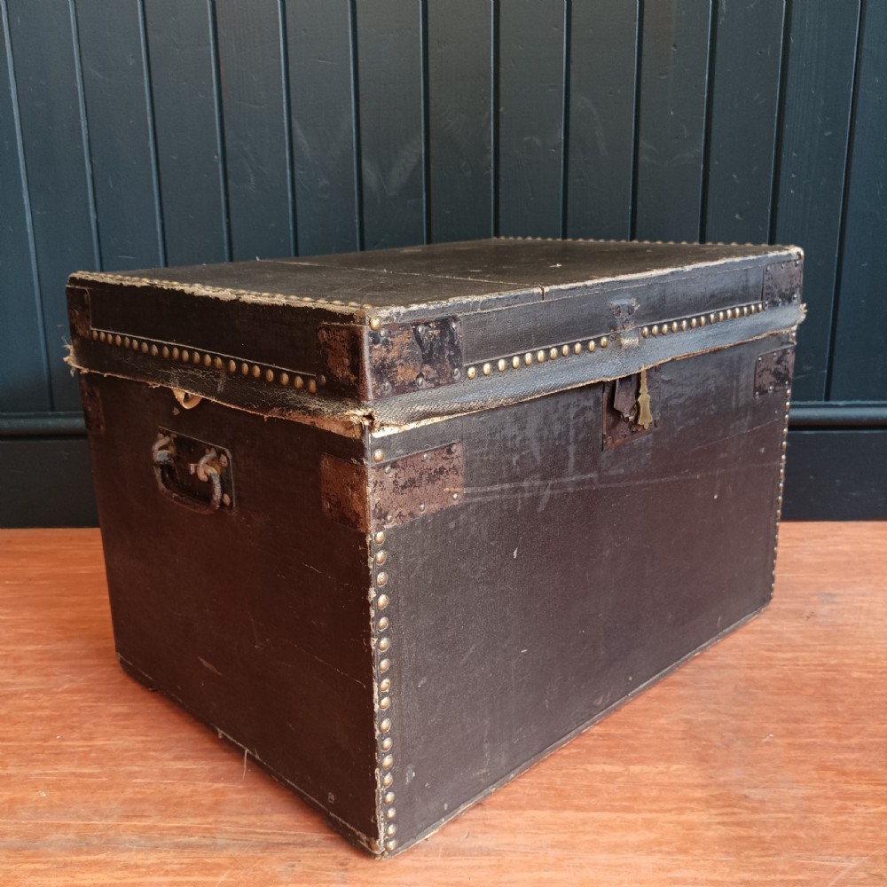 A rectangular dark brown leather campaign trunk featuring brass studding along the lid edges, metal corner brackets, and drop handles. View III
