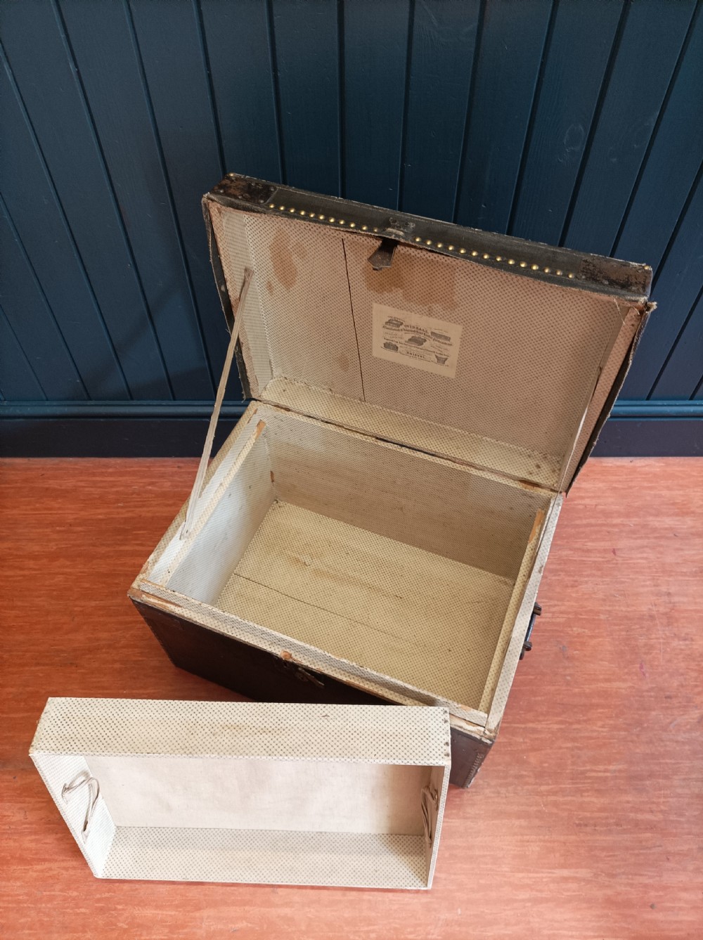 A rectangular dark brown leather campaign trunk featuring brass studding along the lid edges, metal corner brackets, and drop handles. View VI