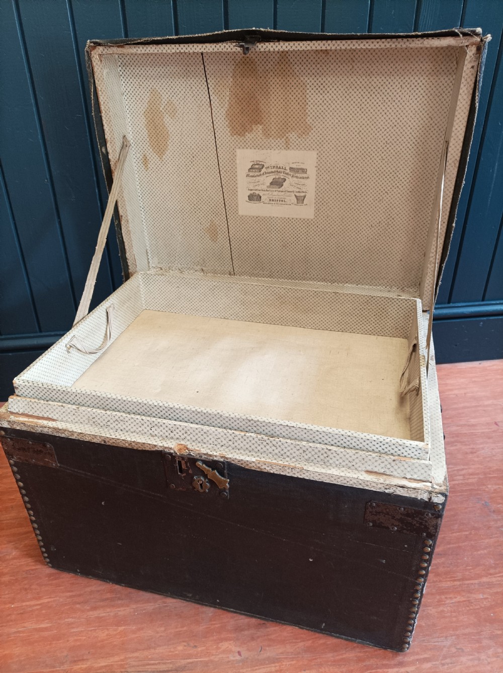 A rectangular dark brown leather campaign trunk featuring brass studding along the lid edges, metal corner brackets, and drop handles. View VII