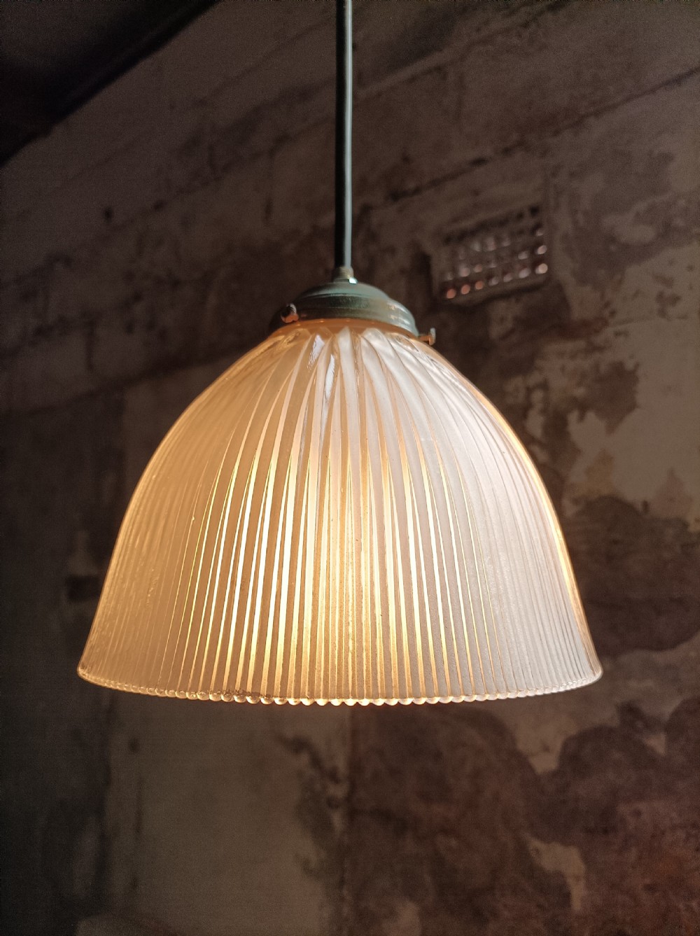 An illuminated clear prismatic glass bell-shaped pendant shade attached to a dark stem with a brass gallery.