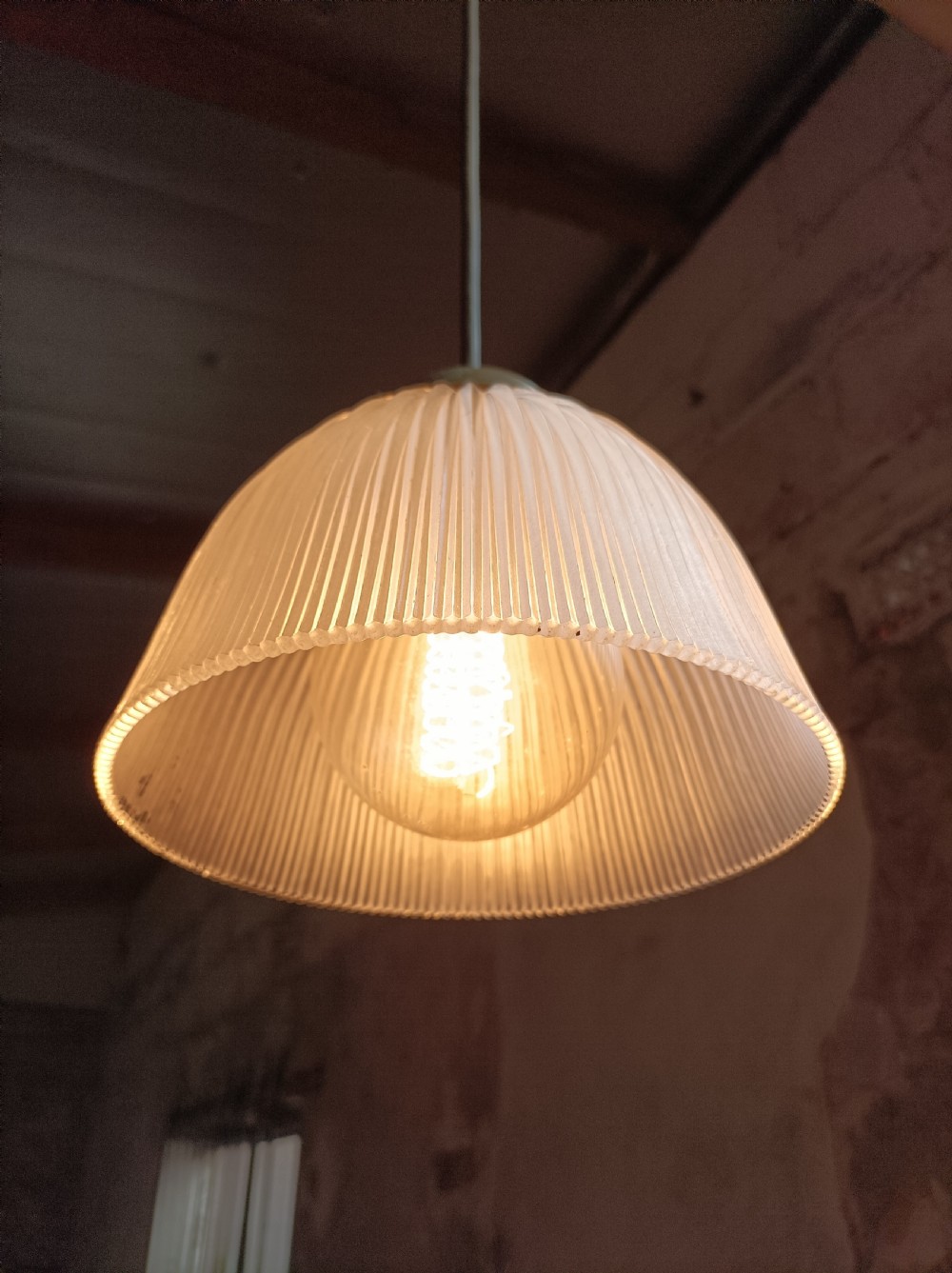An illuminated clear prismatic glass bell-shaped pendant shade attached to a dark stem with a brass gallery. View IV