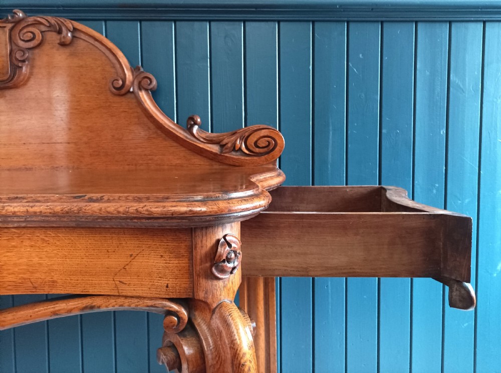 A carved mid-19th-century Victorian oak hall console table featuring scrolled cabriole legs, a central acanthus leaf apron, and a raised gallery back with a carved shield crest. View VI