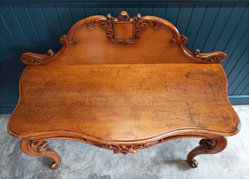 A carved mid-19th-century Victorian oak hall console table featuring scrolled cabriole legs, a central acanthus leaf apron, and a raised gallery back with a carved shield crest. View II