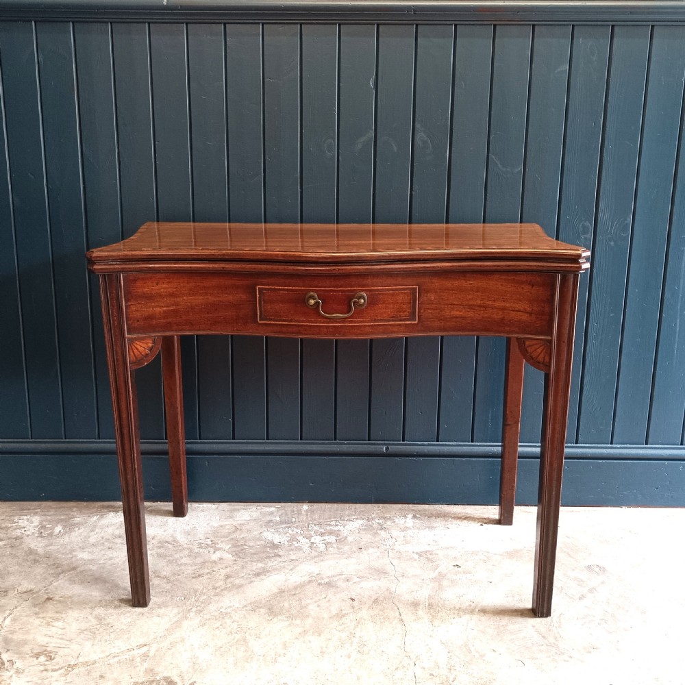 An antique George III mahogany fold-over card table featuring a serpentine front, string inlay, and square tapered legs.
