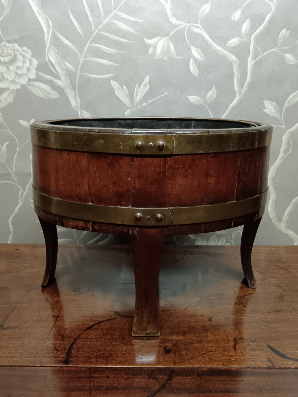 A circular coopered mahogany wine cooler featuring two brass bands and four short splayed legs, containing a metal lining. View II