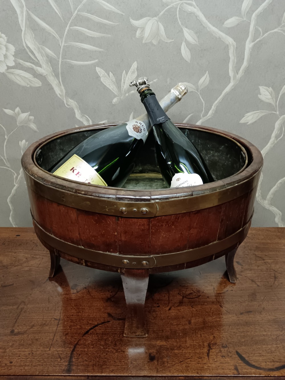 A circular coopered mahogany wine cooler featuring two brass bands and four short splayed legs, containing a metal lining.