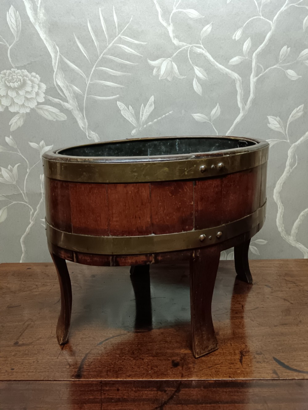 A circular coopered mahogany wine cooler featuring two brass bands and four short splayed legs, containing a metal lining. View X