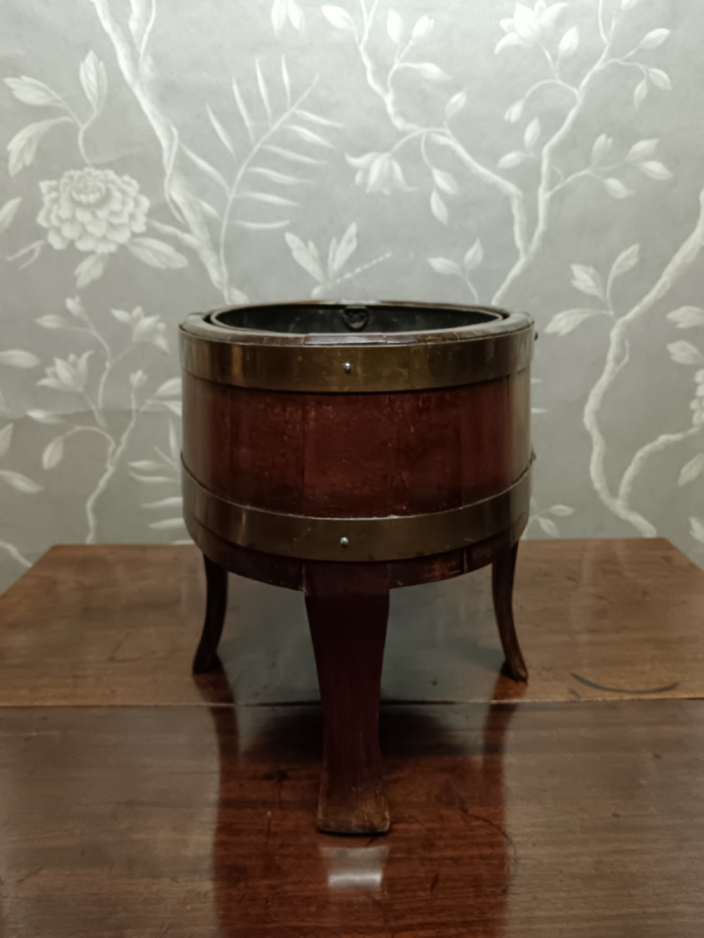 A circular coopered mahogany wine cooler featuring two brass bands and four short splayed legs, containing a metal lining. View XI
