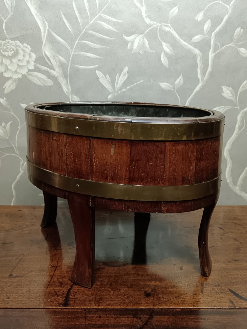A circular coopered mahogany wine cooler featuring two brass bands and four short splayed legs, containing a metal lining. View XII