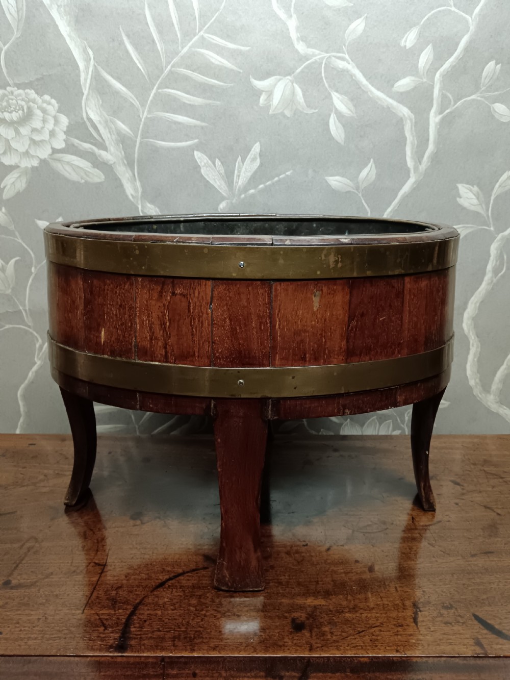 A circular coopered mahogany wine cooler featuring two brass bands and four short splayed legs, containing a metal lining. View XIII