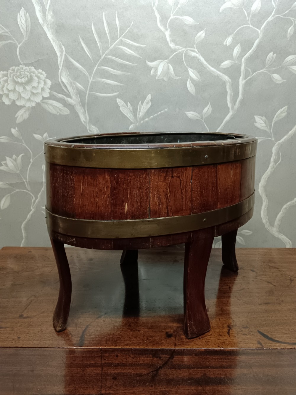 A circular coopered mahogany wine cooler featuring two brass bands and four short splayed legs, containing a metal lining. View XIV