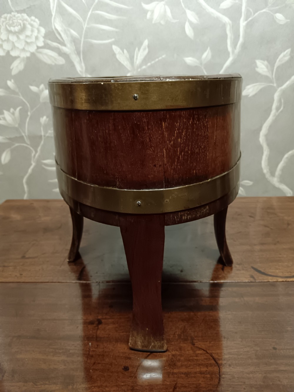 A circular coopered mahogany wine cooler featuring two brass bands and four short splayed legs, containing a metal lining. View XV