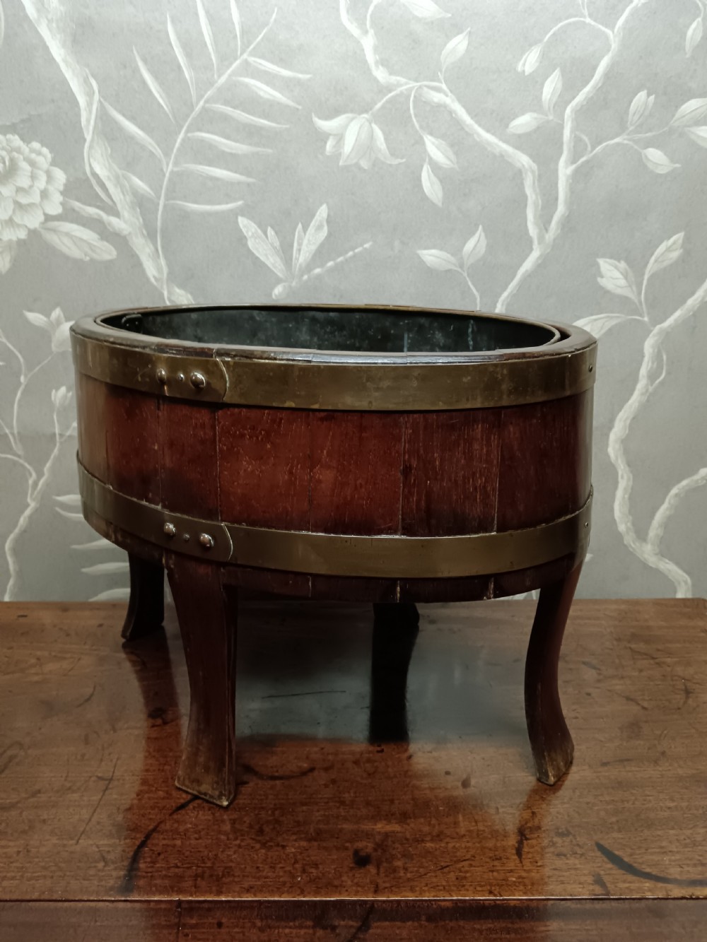 A circular coopered mahogany wine cooler featuring two brass bands and four short splayed legs, containing a metal lining. View XVI