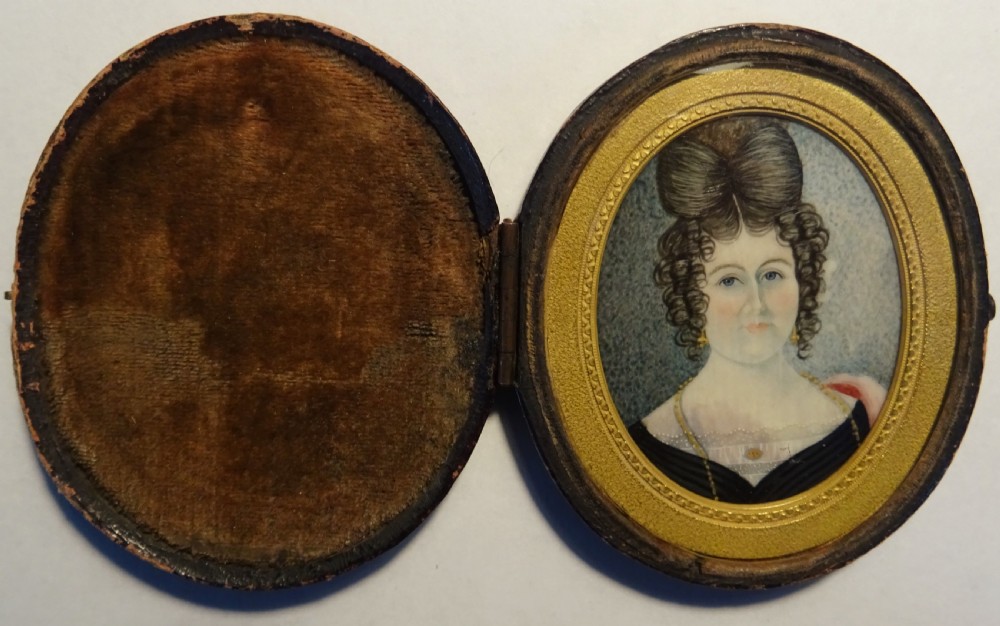 An oval Georgian portrait miniature depicting a lady with elaborate dark hair in an ornate gilt inner border and dark wooden frame. View V