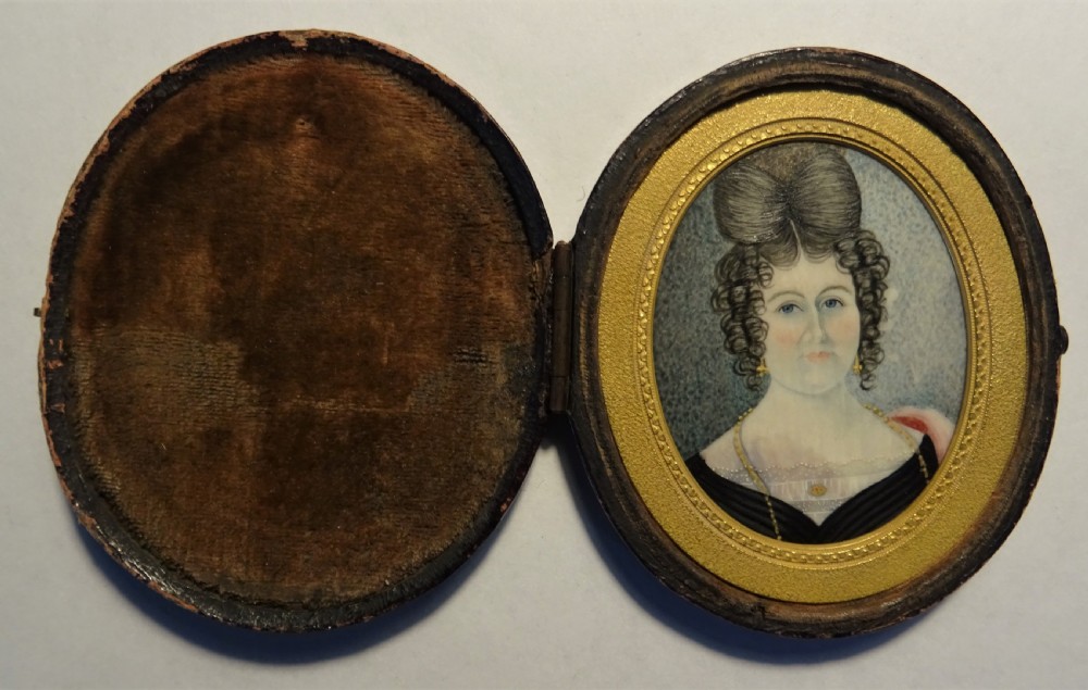 An oval Georgian portrait miniature depicting a lady with elaborate dark hair in an ornate gilt inner border and dark wooden frame. View VII