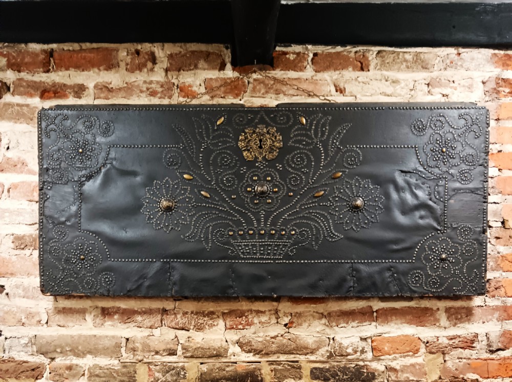 A rectangular dark leather-clad wooden panel adorned with floral and scroll patterns rendered in brass nailhead studs around a central brass escutcheon.