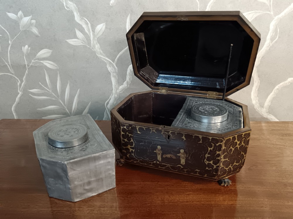 An open octagonal dark lacquer tea box decorated with gilded Chinese motifs containing two engraved pewter metal canisters. View IX