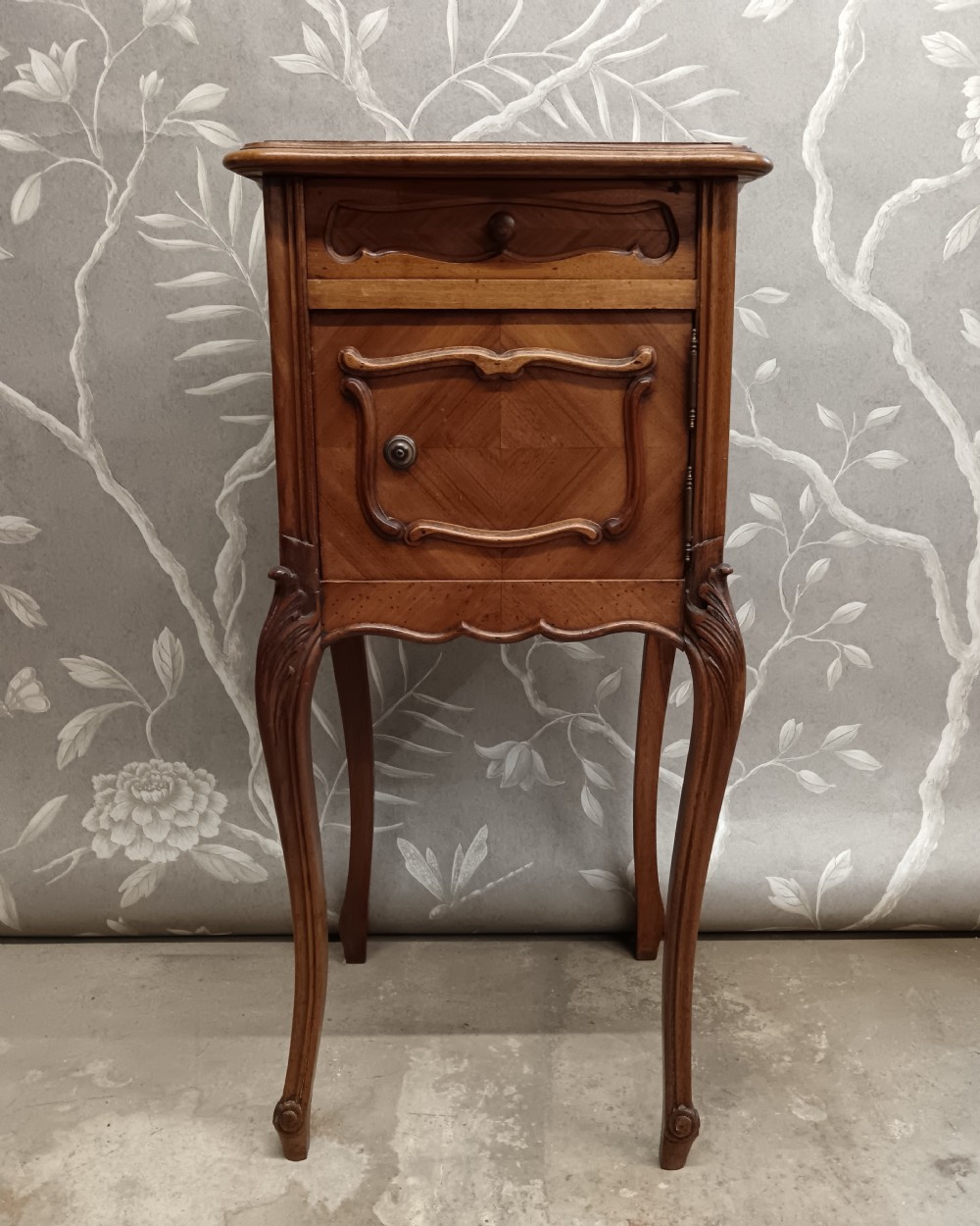 A late 19th-century French walnut bedside cabinet featuring slender cabriole legs, a single top drawer, a cupboard door with parquetry inlay, and carved mouldings.