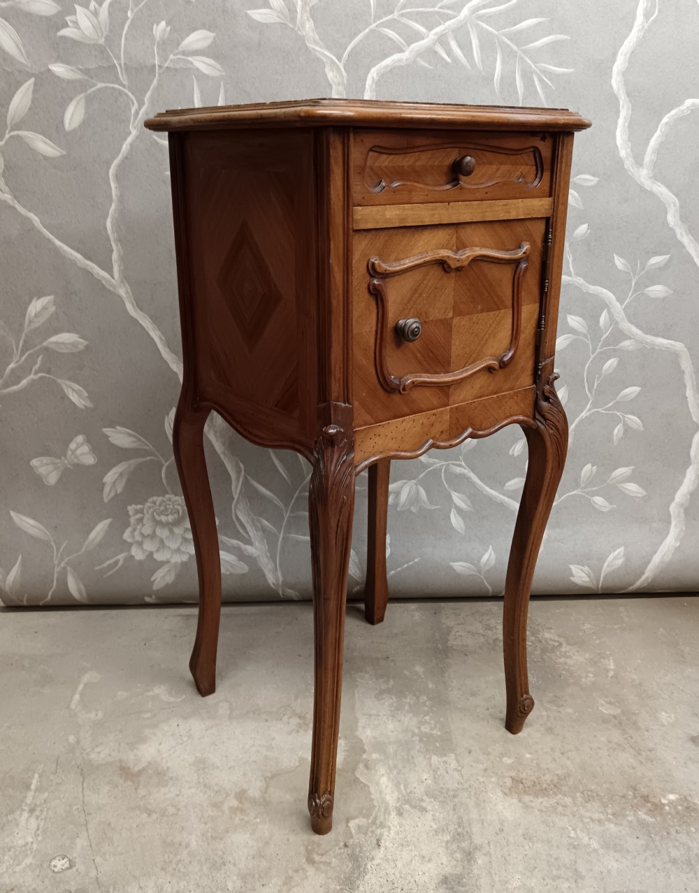 A late 19th-century French walnut bedside cabinet featuring slender cabriole legs, a single top drawer, a cupboard door with parquetry inlay, and carved mouldings. View III