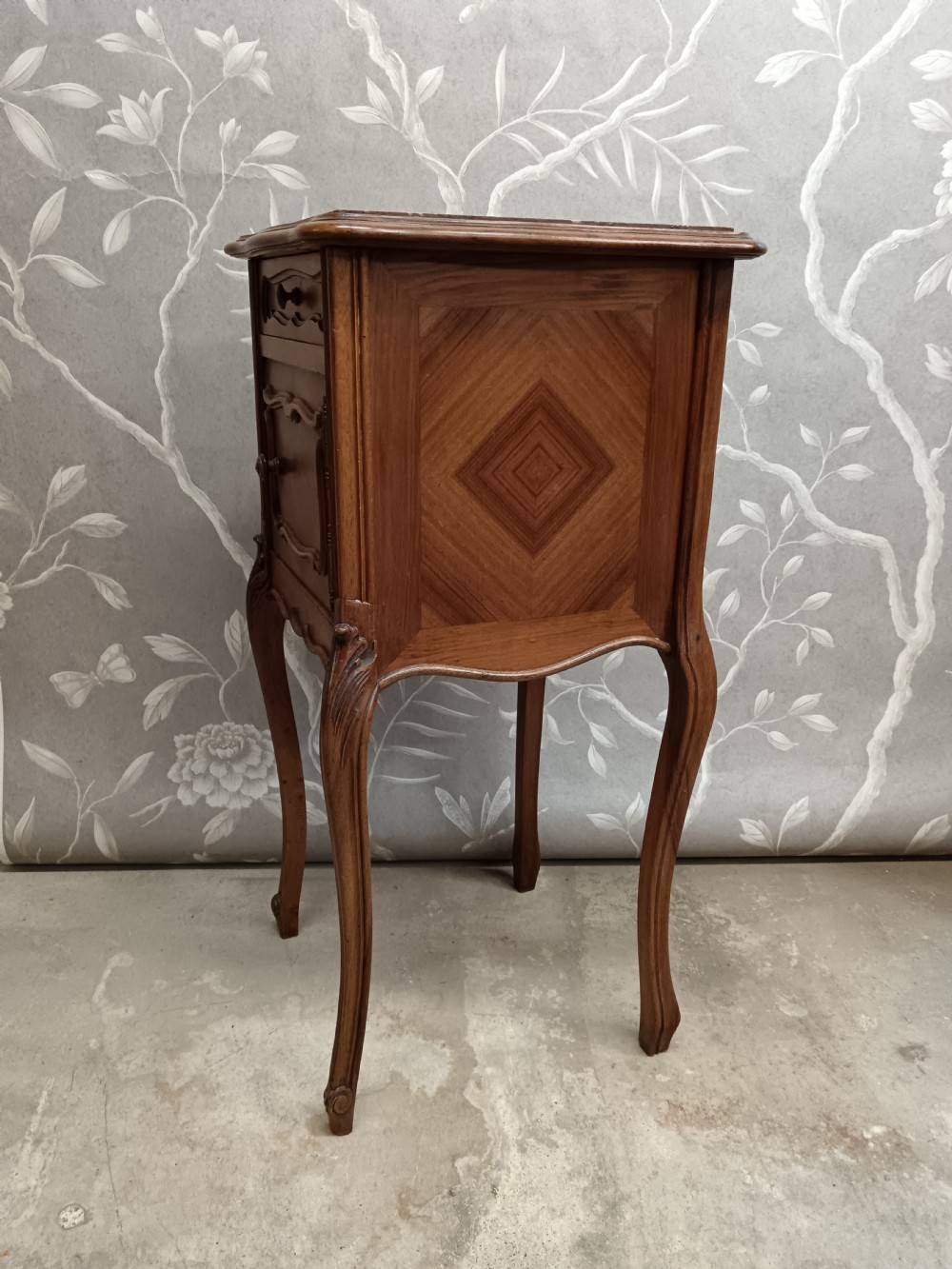 A late 19th-century French walnut bedside cabinet featuring slender cabriole legs, a single top drawer, a cupboard door with parquetry inlay, and carved mouldings. View V