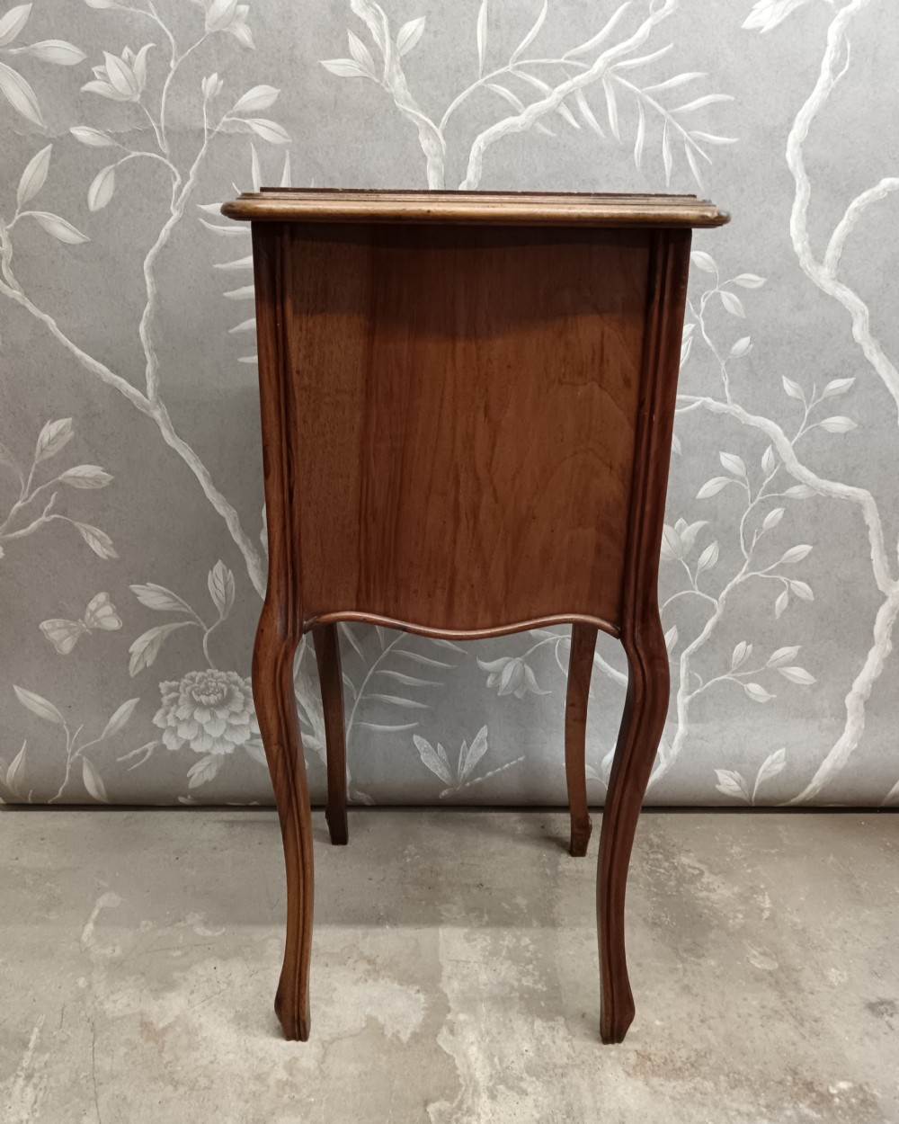 A late 19th-century French walnut bedside cabinet featuring slender cabriole legs, a single top drawer, a cupboard door with parquetry inlay, and carved mouldings. View VI