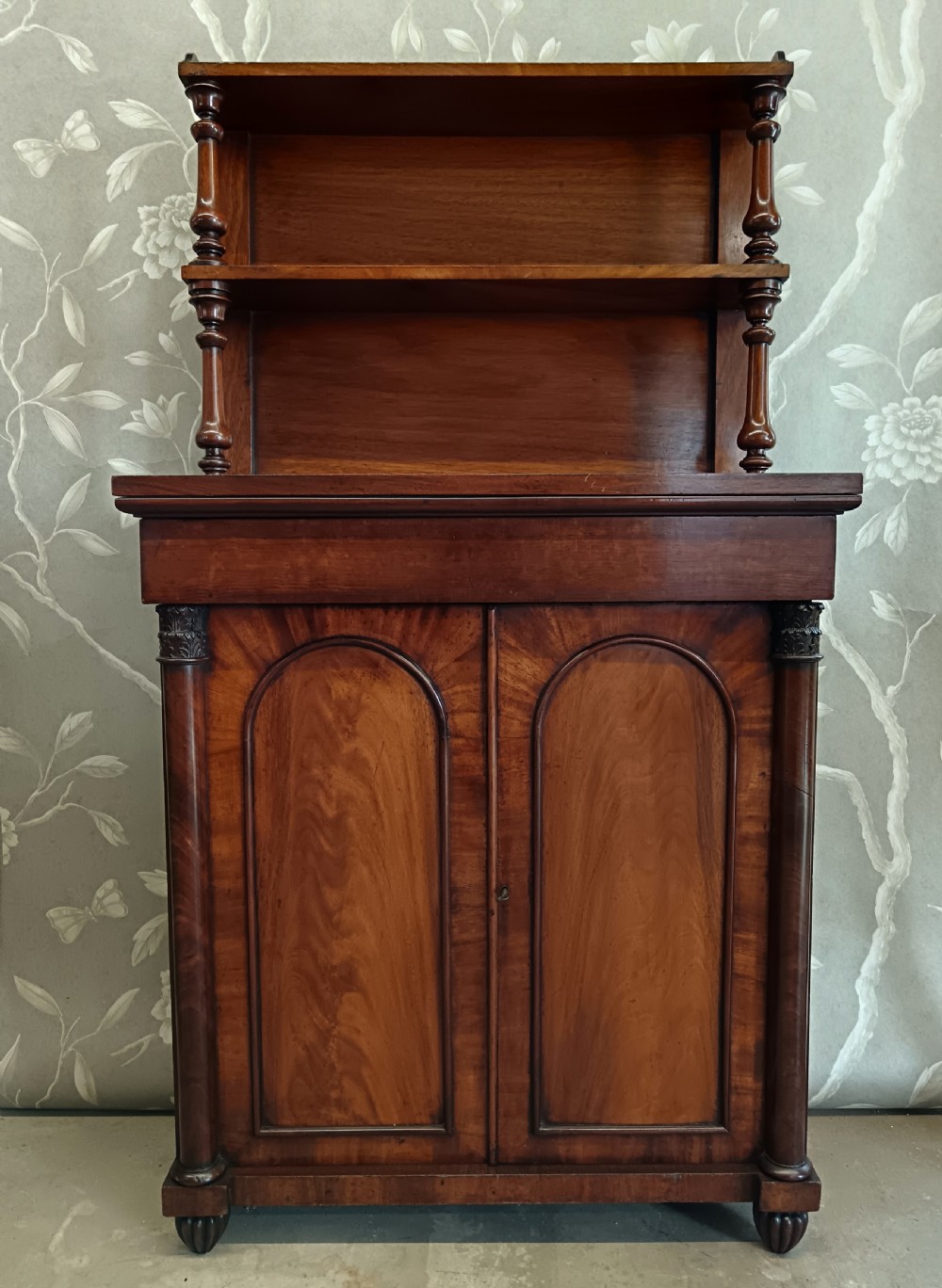 A Regency mahogany chiffonier featuring a two-tier open shelf superstructure above a two-door lower cabinet with arched panel doors and turned columns.