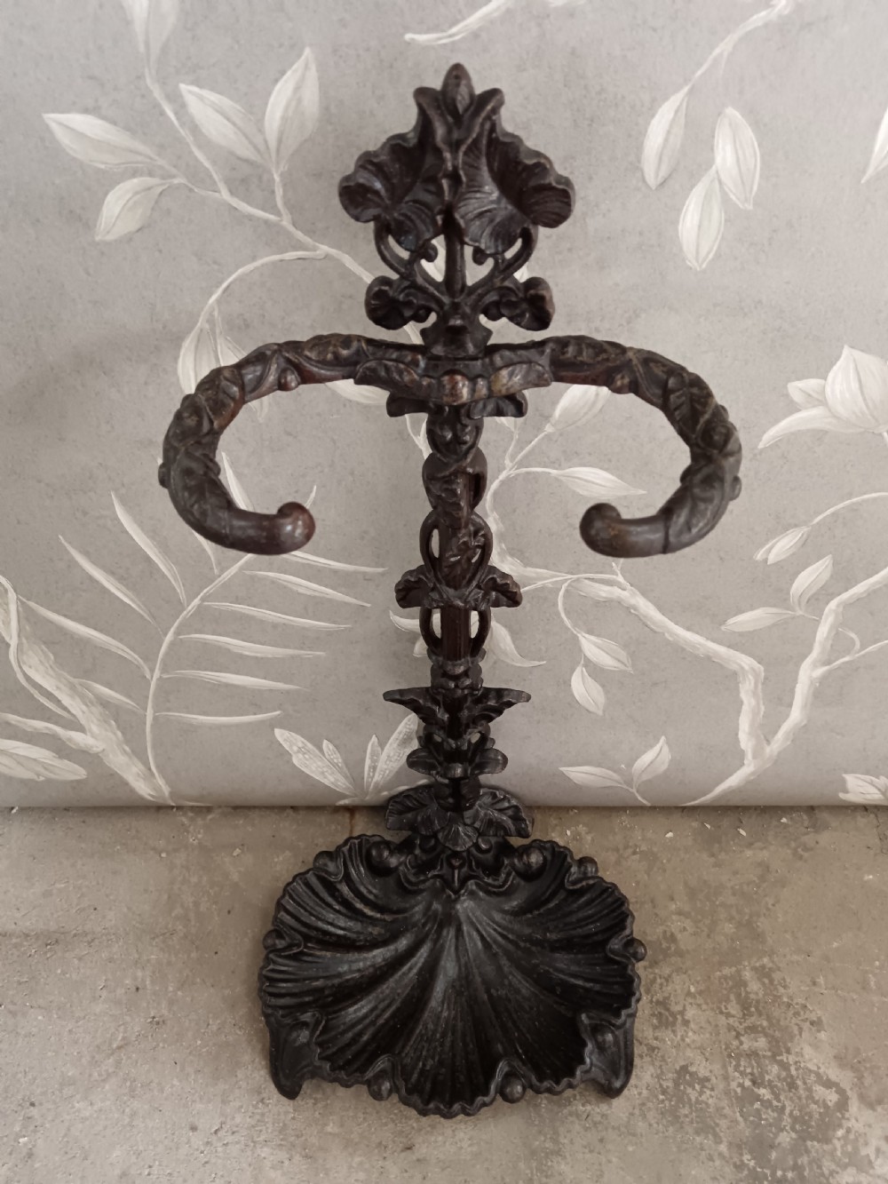 A dark cast iron Art Nouveau umbrella stand featuring stylized floral fretwork, dual upper loops, and a shell-shaped drip tray base. View II