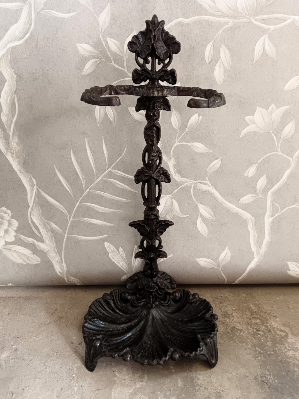 A dark cast iron Art Nouveau umbrella stand featuring stylized floral fretwork, dual upper loops, and a shell-shaped drip tray base.