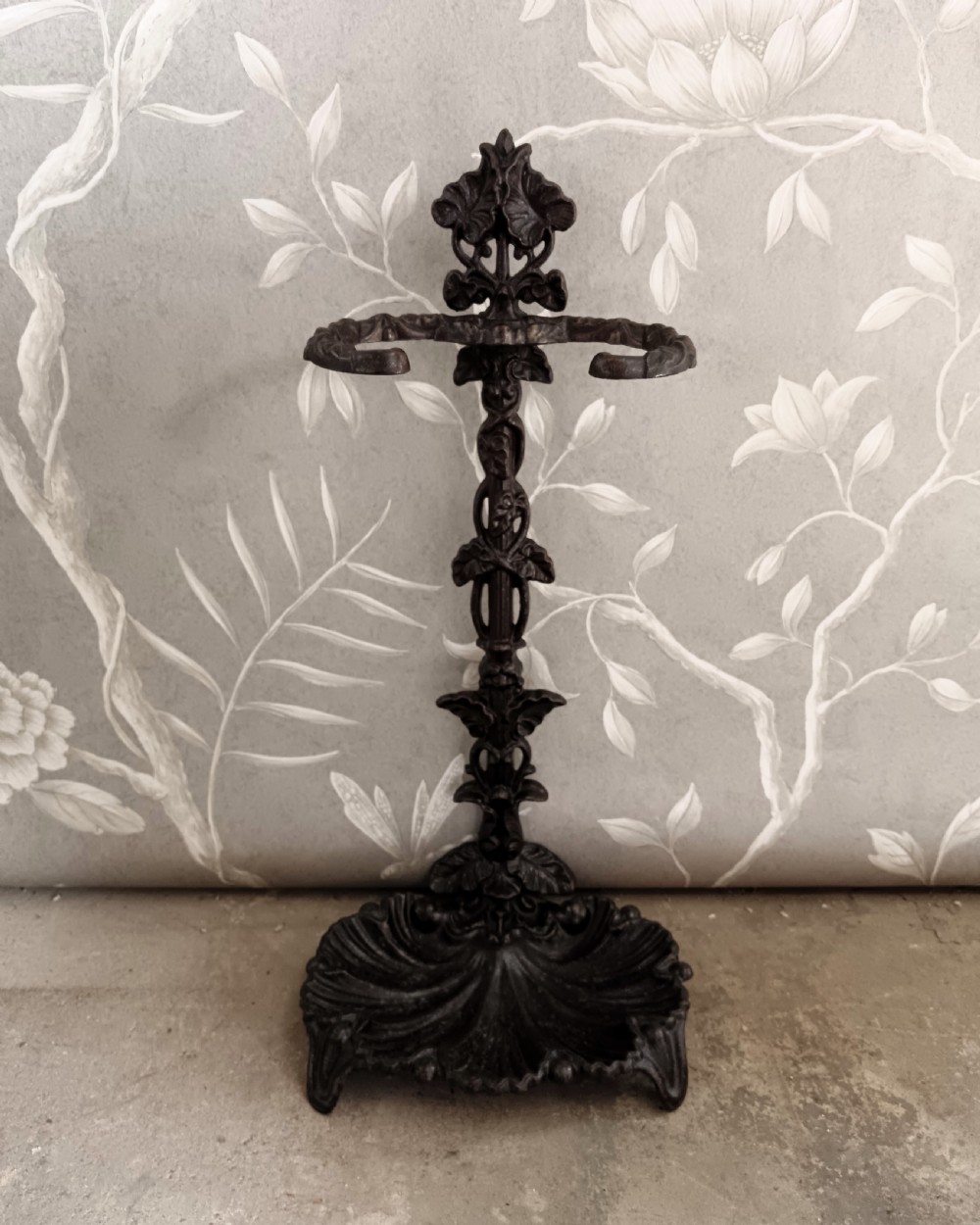 A dark cast iron Art Nouveau umbrella stand featuring stylized floral fretwork, dual upper loops, and a shell-shaped drip tray base. View III