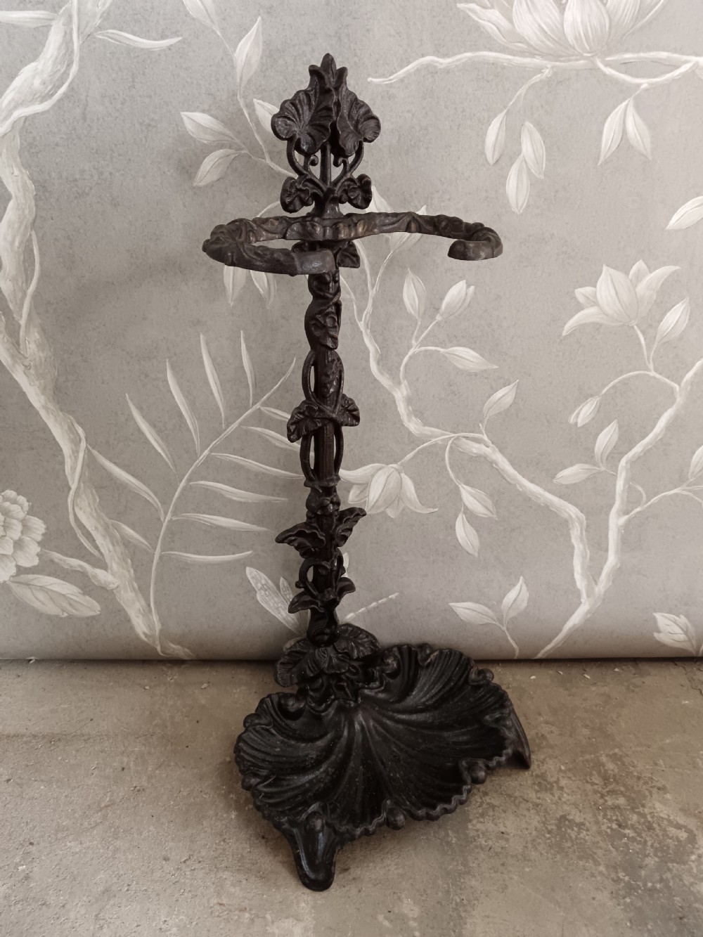 A dark cast iron Art Nouveau umbrella stand featuring stylized floral fretwork, dual upper loops, and a shell-shaped drip tray base. View V