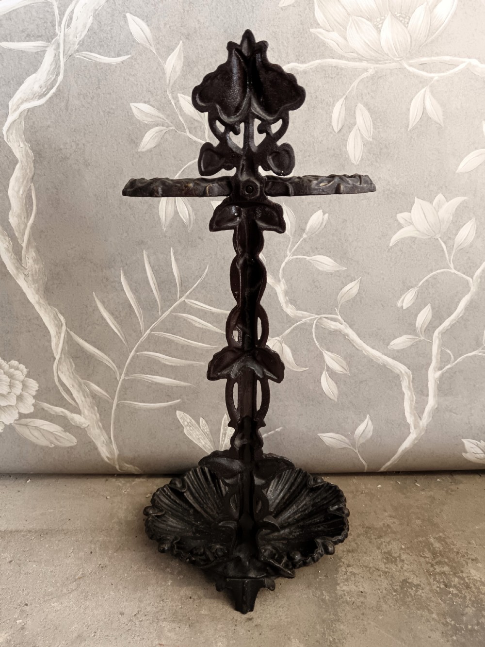 A dark cast iron Art Nouveau umbrella stand featuring stylized floral fretwork, dual upper loops, and a shell-shaped drip tray base. View VII