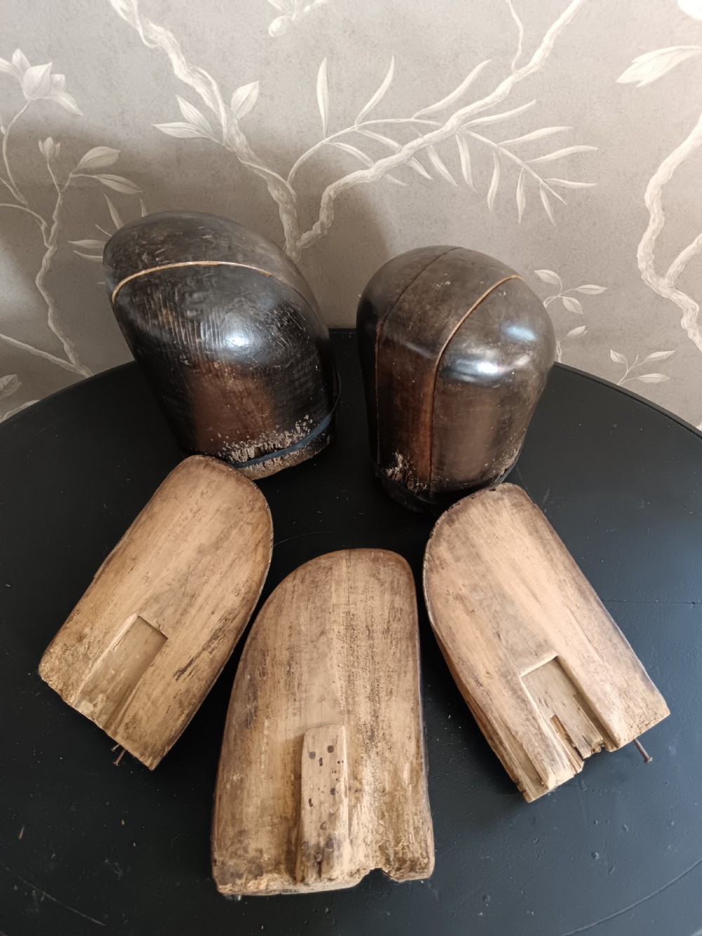 Three tall carved dark wooden millinery hat blocks with sloping rounded tops arranged in a row on a surface. View III