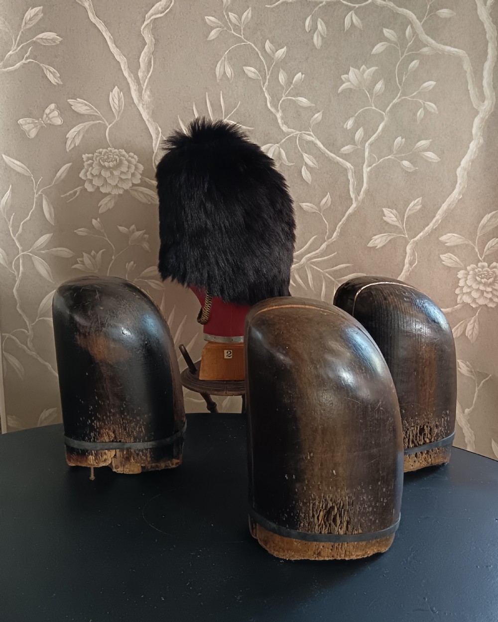 Three tall carved dark wooden millinery hat blocks with sloping rounded tops arranged in a row on a surface. View VI