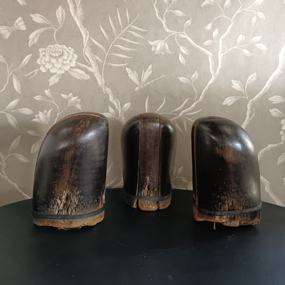 Three tall carved dark wooden millinery hat blocks with sloping rounded tops arranged in a row on a surface. View VIII