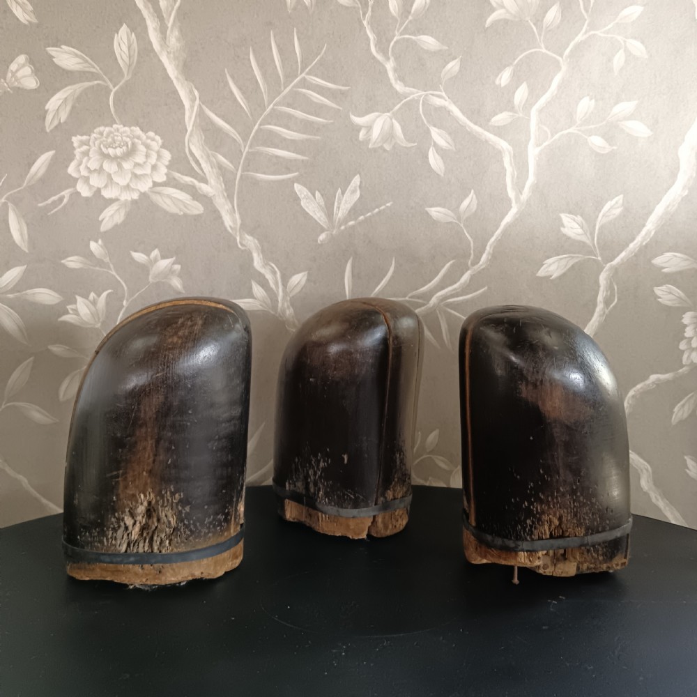 Three tall carved dark wooden millinery hat blocks with sloping rounded tops arranged in a row on a surface. View IX