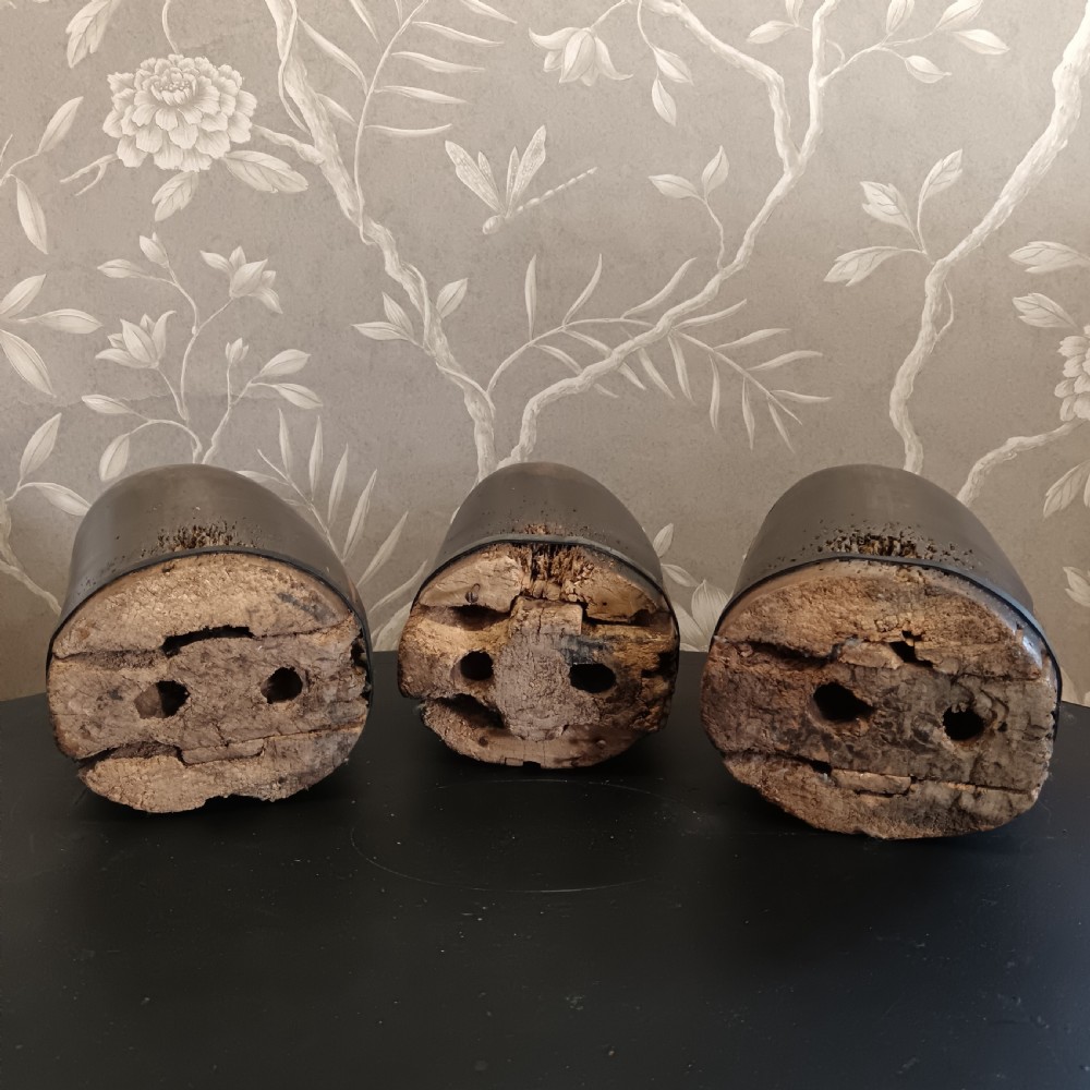 Three tall carved dark wooden millinery hat blocks with sloping rounded tops arranged in a row on a surface. View XII