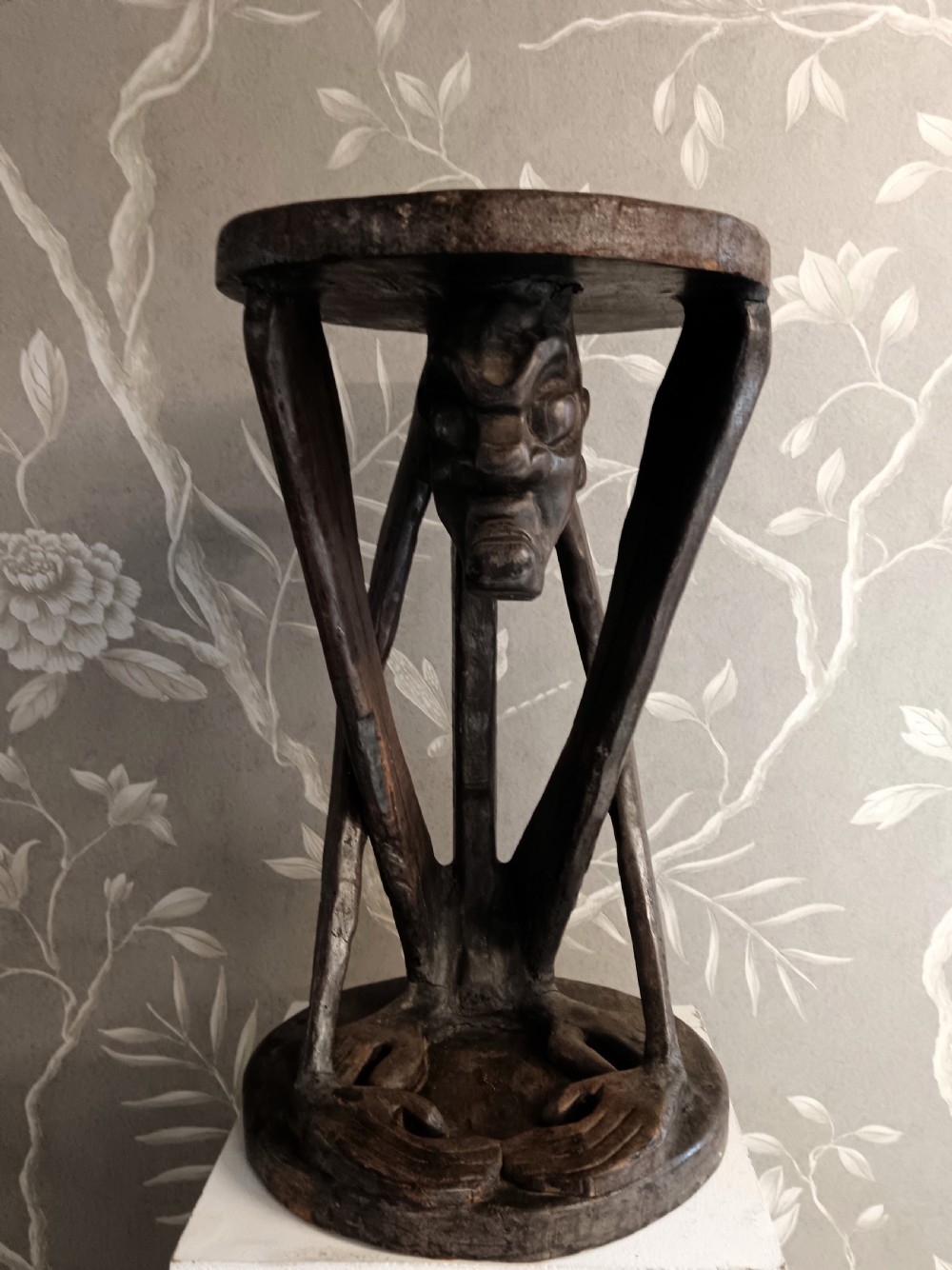 A dark carved timber side table featuring a circular top supported by a stylised crouching figure above a rounded base. View II