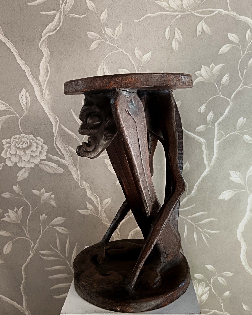A dark carved timber side table featuring a circular top supported by a stylised crouching figure above a rounded base. View III
