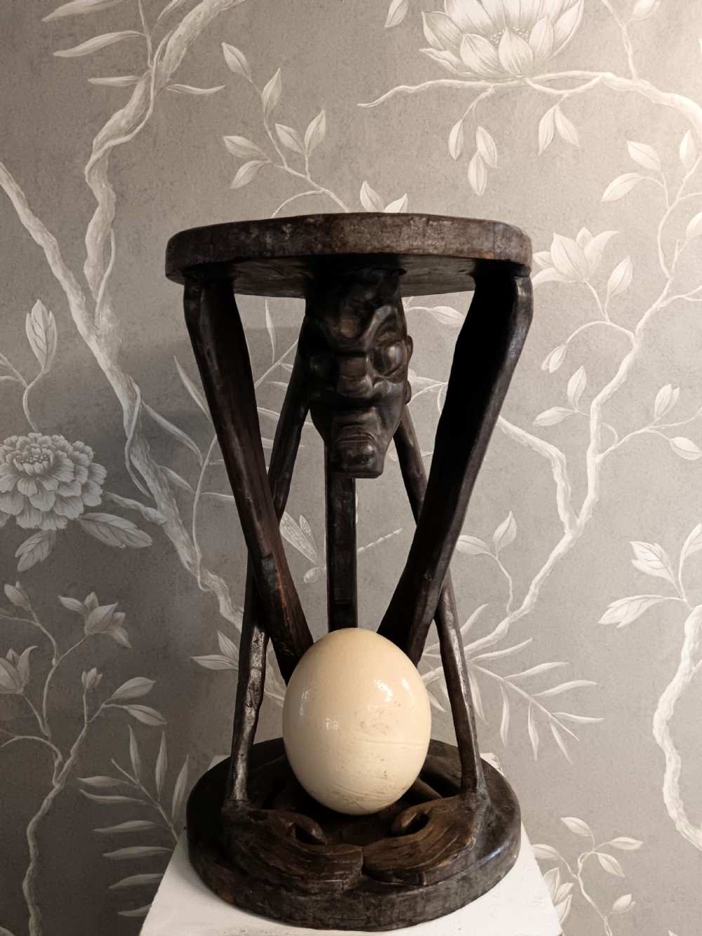 A dark carved timber side table featuring a circular top supported by a stylised crouching figure above a rounded base. View V