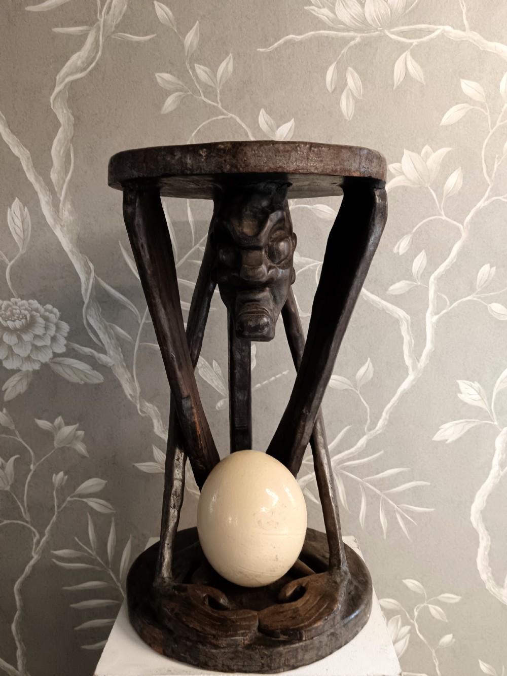 A dark carved timber side table featuring a circular top supported by a stylised crouching figure above a rounded base. View VI