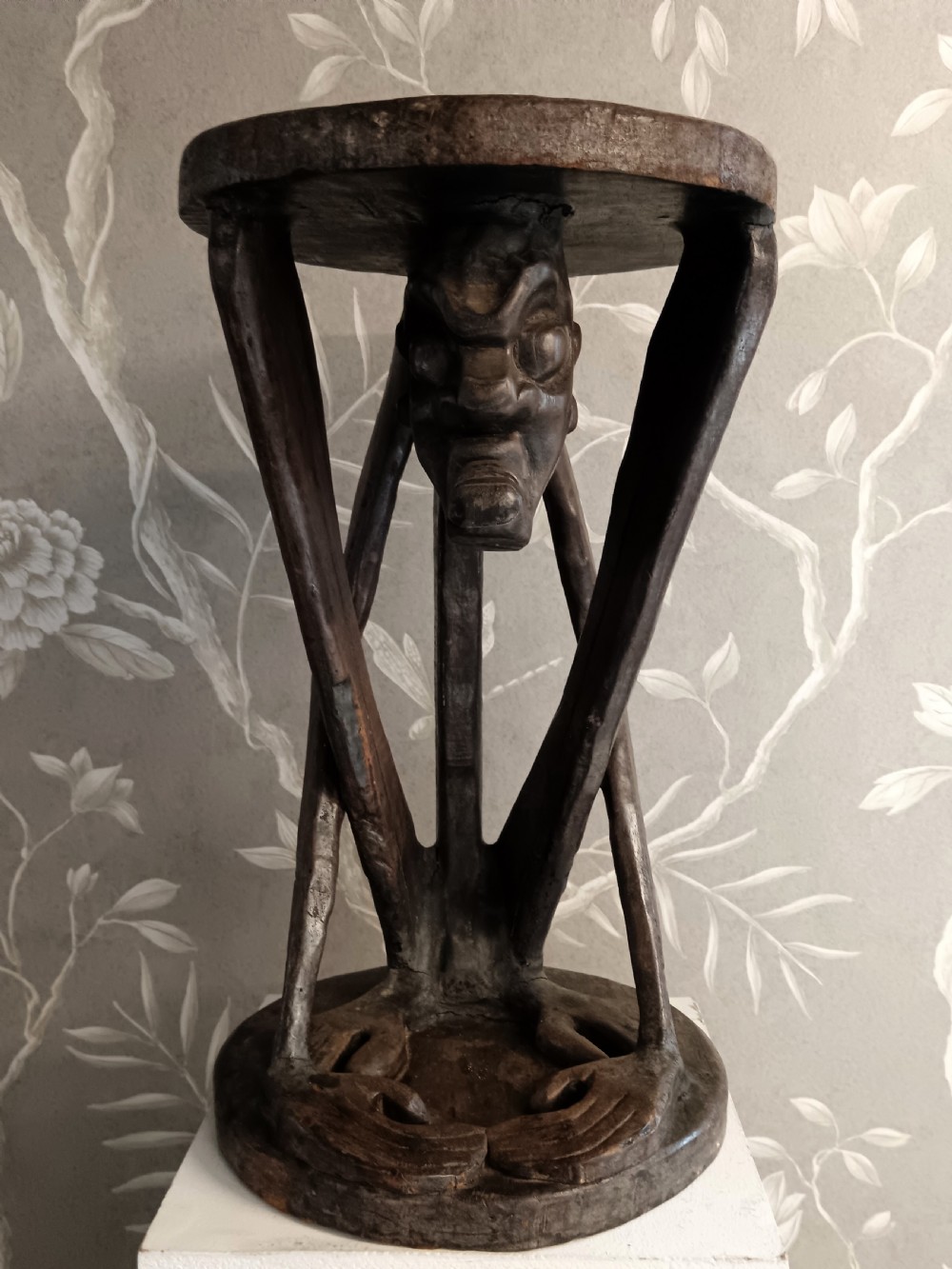 A dark carved timber side table featuring a circular top supported by a stylised crouching figure above a rounded base. View VIII